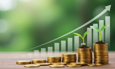 A vibrant, motivational image showing a seedling growing from a stack of coins, with a bright, upward-trending graph in the background. Description: Foreground: A small green seedling sprouting from a pile of gold coins, symbolizing money growing through smart investments. Background: A clean, modern graph or chart with an upward arrow, representing financial growth and success. Color Palette: Bright greens (growth), golds (wealth), and blues (trust and stability) to evoke positivity and confidence. Style: Clean, minimalist, and professional with a touch of warmth to appeal to a general audience.